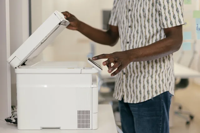 Person operating photocopier in modern office setting, engaging with technology. Comparing document scanners with multifunction devices