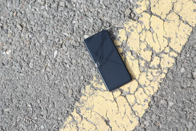 A close-up view of a cracked smartphone lying on a sunlit asphalt road. Protecting work data on a lost phone